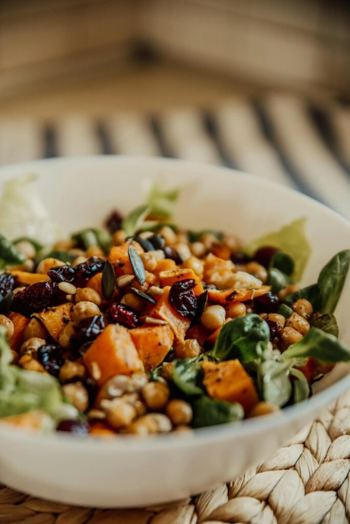 Close-up of a vibrant chickpea, sweet potato, and greens salad with cranberries and seeds.